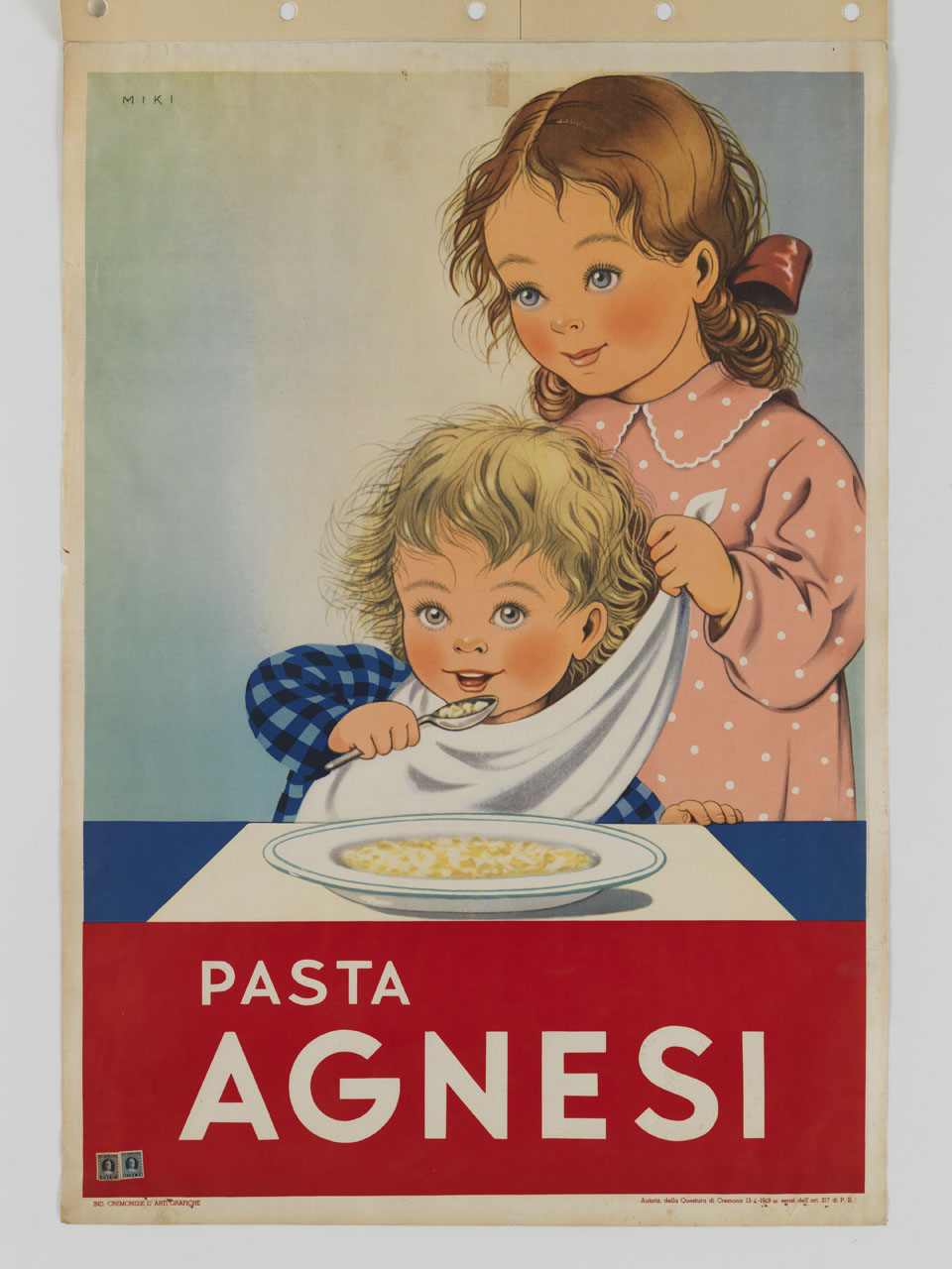 un bambino si porta alla bocca un cucchiaio di pasta mentre una bambina gli annoda un tovagliolo al collo (manifesto) di MIKI - ambito italiano (sec. XX)