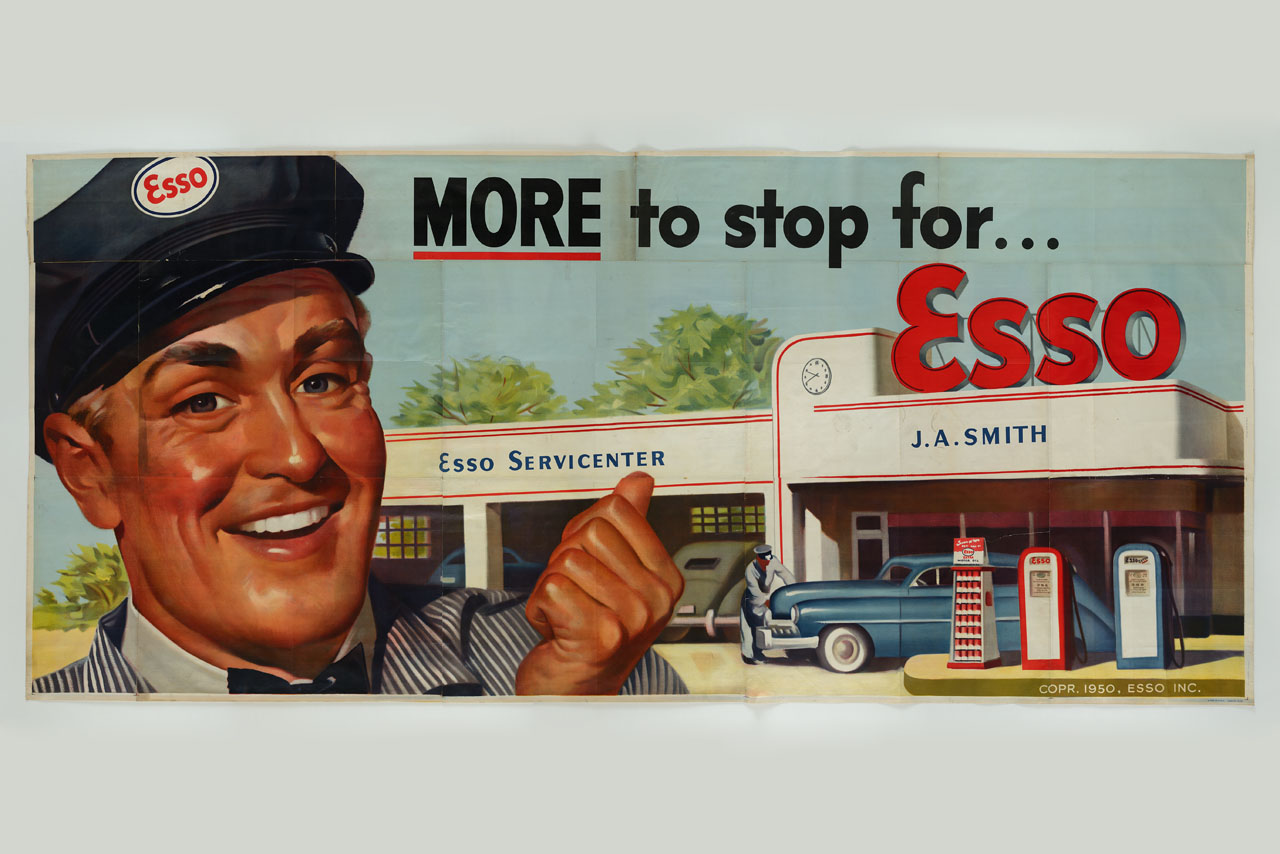 uomo in divisa Esso sorride invitante e indica la stazione di servizio (manifesto, stampa composita) - ambito americano (sec. XX)